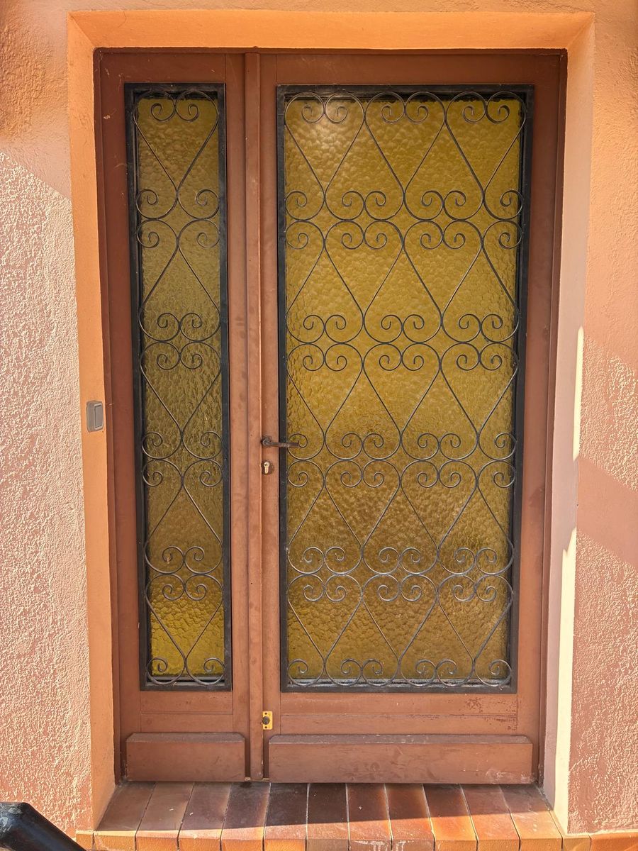 Ancienne porte d'entrée en bois avec grille en fer forgé et vitrage jaune